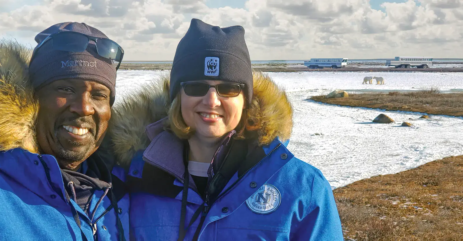 Two travelers on the tundra with polar bears and tundra vehicles behind